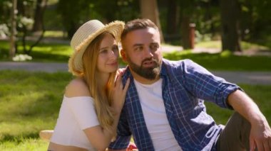 Yaz parkında piknik yapmaktan hoşlanan erkek ve kadın, birlikte konuşmak, yeşil çimenlerde oturmak ve yan bakmak.