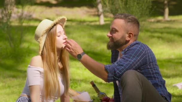 Un picnic romántico. Amando hombre de mediana edad alimentando a su amada esposa con fresas frescas y besándola en el soleado parque — Vídeo de stock