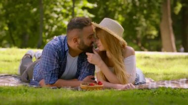 Aşk ve şefkat kavramı. Yaz parkında yeşil çimlerde dinlenen, birbirini öpen mutlu bir adam ve kadın.