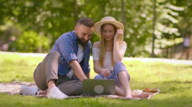 Kaygısız orta yaşlı adam ve kadın yeşil yaz parkında pikniğin tadını çıkarıyorlar, internette internette sörf yapıyorlar, ağır çekimde.