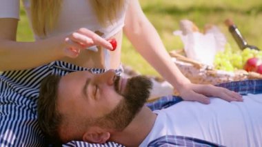 Piknikte aşk oyunları. Kadın dizlerinin üzerine çöküp, kocasını taze çilekle besleyen rahat bir adam.