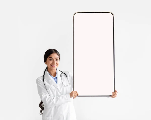 Kadın doktor elinde büyük beyaz bir akıllı telefon ekranı tutuyor. — Stok fotoğraf