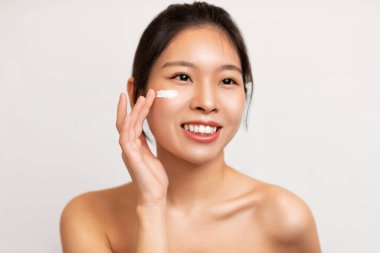 Asyalı bir kadının güzel portresi yanağına krem sürüyor.