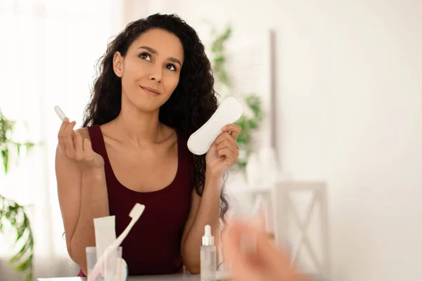 Thoughtful young woman making choice of menstruation hygiene product near mirror at home, free space — Stock Photo, Image