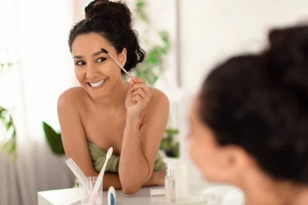 Beautiful young woman applying mascara, looking in mirror at bathroom, blank space — Stock Photo, Image