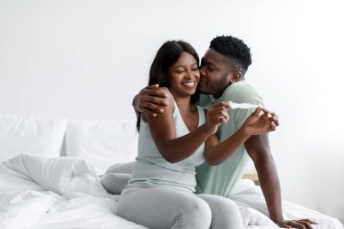 Mutlu yıllar Afro-Amerikan koca karısını öpüyor hamilelik testinin pozitif sonucunu kutluyor.