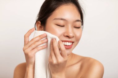 Genç Asyalı kadın yüzünü havluyla ovuyor.