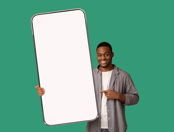 Отличное мобильное предложение. Счастливый черный мужчина указывает на огромный пустой смартфон в руке, показывая макет для вашего дизайна — стоковое фото