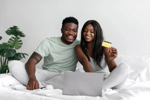 Χαρούμενος νεαρός αφροαμερικάνος σύζυγος και σύζυγος που κοιτάζει το lap-top και δείχνει την πιστωτική κάρτα, ψωνίζοντας on-line — Φωτογραφία Αρχείου