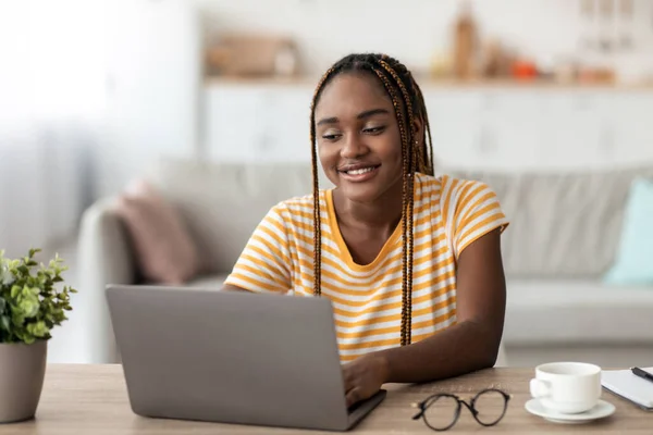 Mujer negra positiva freelancer trabajando en el ordenador portátil en casa —  Fotos de Stock