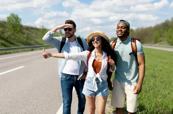 快乐的多种族青年朋友站在高速公路上，竖起大拇指，搭便车，一起上路 — 图库照片