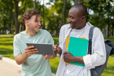Lise öğrencileri. Dersten sonra parkta ya da kampüste yürüyen mutlu beyaz ve Afrikalı Amerikalı erkek arkadaşlar.