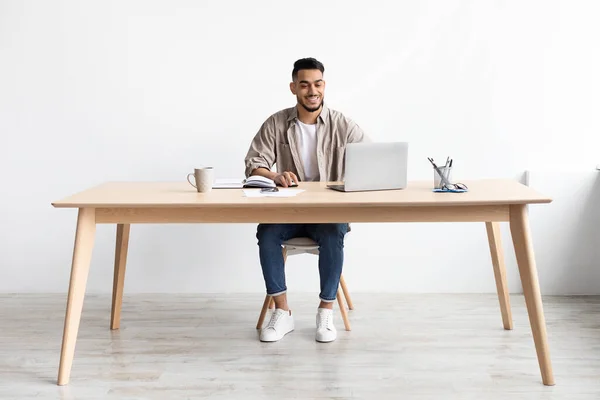 Sorridente uomo arabo utilizzando il computer portatile seduto alla scrivania in ufficio — Foto Stock
