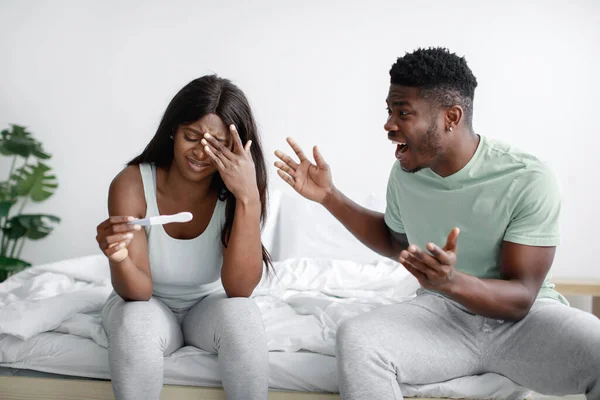 Irritado milenar Africano americano marido gritando com triste esposa com teste de gravidez no interior do quarto — Fotografia de Stock