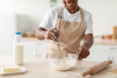 Gülümseyen bin yıllık Afro-Amerikan kadın önlüklü. Minimalist mutfak iç mekanında turta için hamur hazırlıyor.