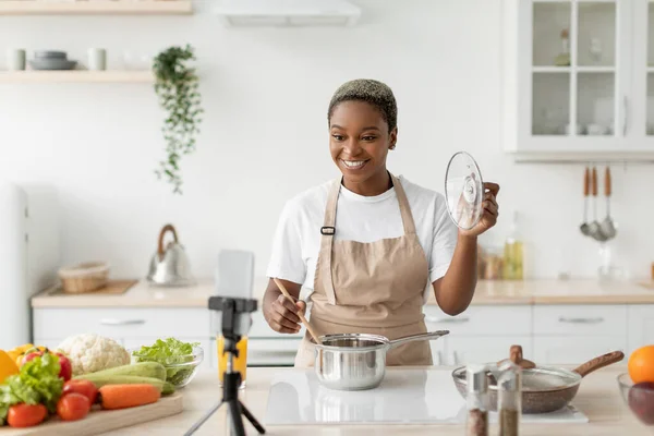 Cheerful millennial african american female in apron preparing food and making video lesson — Stock Photo, Image