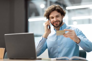 Gülümseyen adam kredi kartıyla akıllı telefondan konuşuyor.