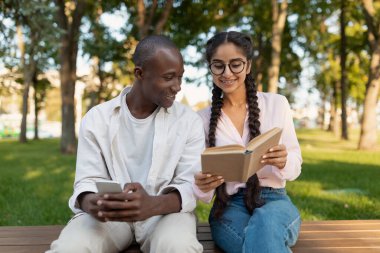 Kampüste dinlenen neşeli çok ırklı öğrenciler, erkek arkadaşına kitap gösteren ve dışarıda dersleri tartışan bir kız.