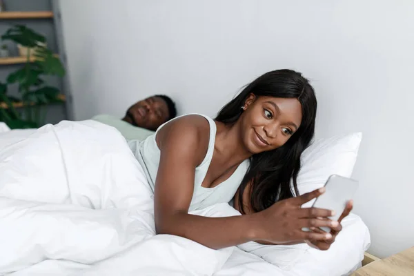 Έκπληκτη χαρούμενη νεαρή Αφροαμερικανή σύζυγος κοιτάζοντας smartphone στο κρεβάτι σε λευκό υπνοδωμάτιο εσωτερικό — Φωτογραφία Αρχείου