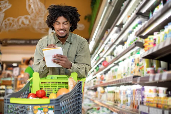 Negro chico celebración de compras lista tomando notas en supermercado —  Fotos de Stock