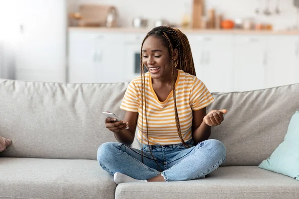 Alegre millennial mujer negra que se enfría en casa con el teléfono inteligente —  Fotos de Stock