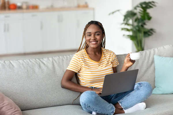 Hübsche schwarze Dame sitzt auf Couch mit Laptop, Kopierraum — Stockfoto