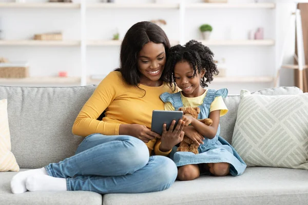 Веселая молодая афроамериканская мама и маленькая дочь расслабляются с цифровой таблеткой — стоковое фото