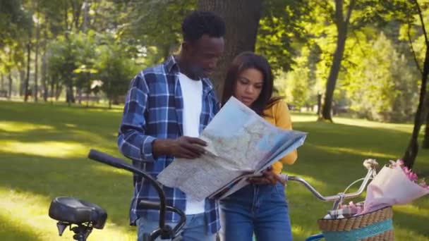 Молодая африканская пара изучает карту, планирует маршрут через парк, наслаждается поездкой на велосипедах, отслеживает выстрел — стоковое видео
