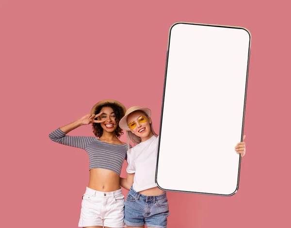 Två attraktiva multietniska kvinnor visar mobiltelefon med tom skärm — Stockfoto