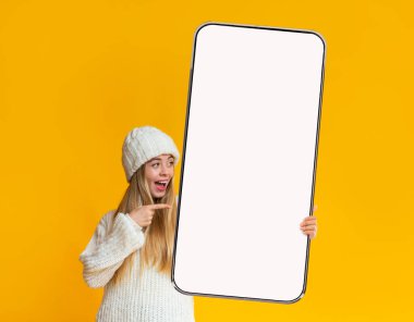 Duygusal sarışın kadın elinde kocaman, boş ekranlı bir akıllı telefon tutuyor.