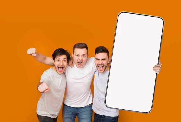 Drei glückliche Millennial-Freunde zeigen Smartphone mit leerem Bildschirm — Stockfoto