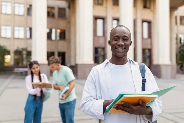 Pożyczki na edukację. Portret afrykańskiego studenta płci męskiej pozującego w pobliżu budynku uniwersyteckiego — Zdjęcie stockowe