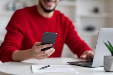 Arap adam dizüstü bilgisayarla masada otururken modern cep telefonu kullanıyor.