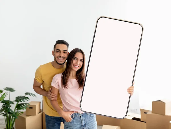 Junges Paar zeigt großes Smartphone mit leerem Bildschirm, Immobilienanzeige oder App zur Bestellung der Lieferung — Stockfoto