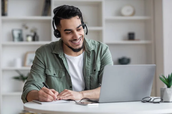 Enseñanza a distancia. Hombre árabe en el estudio de auriculares en línea con el ordenador portátil en casa —  Fotos de Stock