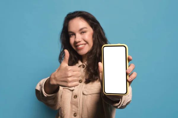 Froh glücklich junge hübsche Europäerin zeigt Smartphone mit leerem Bildschirm und Daumen hoch — Stockfoto