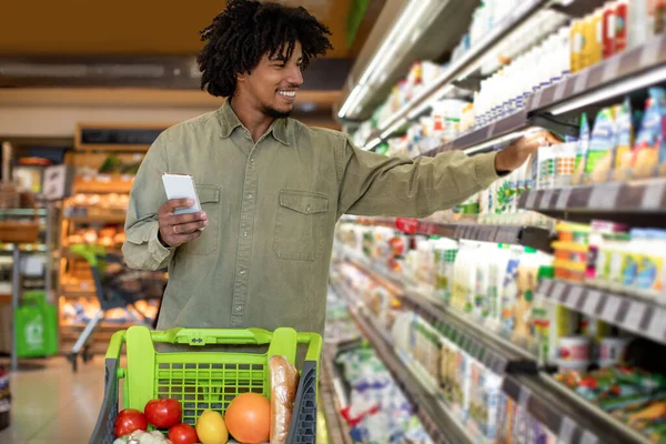 Afroamerykanin robi zakupy spożywcze trzymając komórkę w supermarkecie — Zdjęcie stockowe