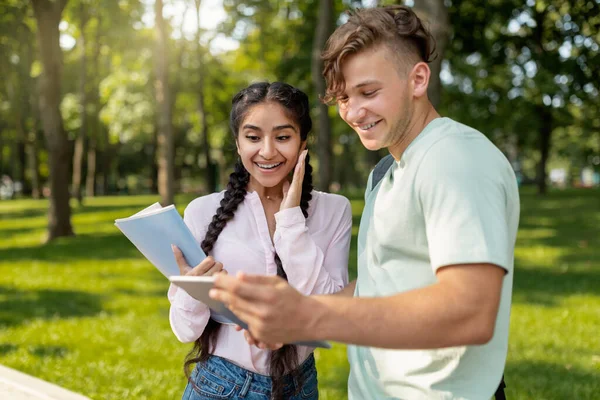 Estudiantes multirraciales muy alegres revisando los resultados del examen en una tableta digital y sonriendo, caminando por el parque o el campus universitario — Foto de Stock