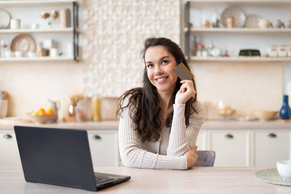 Gelukkig dromerige vrouw met behulp van moderne laptop, met een creditcard en glimlachen, denken wat te kopen terwijl u thuis blijft — Stockfoto