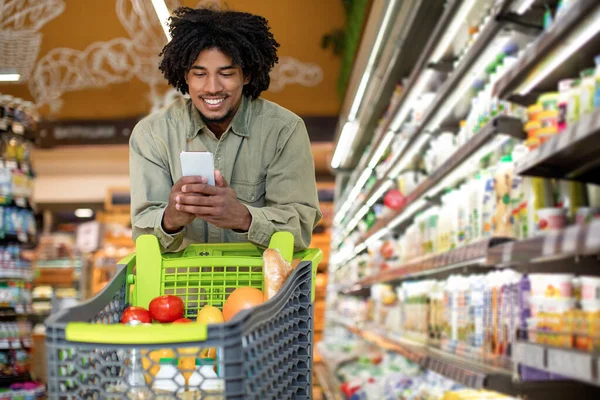 Glada afrikanska Male Använda Mobiltelefon Göra Livsmedel Shopping I Lager — Stockfoto