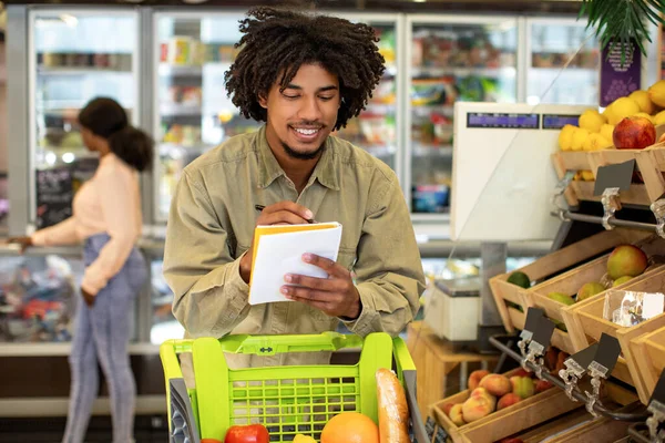 Glad afroamerikansk man skriver mataffär Shopping List I snabbköpet — Stockfoto