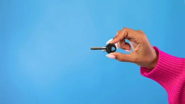 Cropped view of young black woman holding metal house key on blue studio background, panorama with copy space — Stock Photo, Image