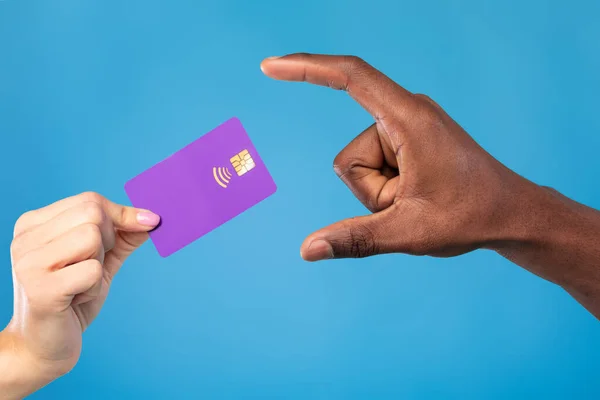 Zbliżenie widok młodej kobiety daje kartę kredytową Afroamerykaninowi na tle niebieskiego studia — Zdjęcie stockowe