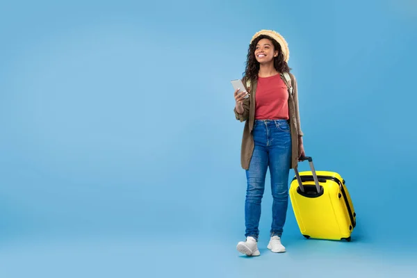 Jonge zwarte vrouw met koffer met smartphone, boeking hotel of vakantie online, met behulp van web reisbureau app — Stockfoto