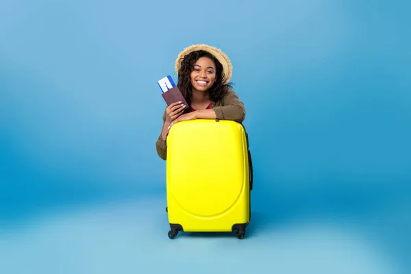 Šťastná černoška v neformálním oblečení sedí za kufrem, drží pas a letenky, jede na letní dovolenou — Stock fotografie