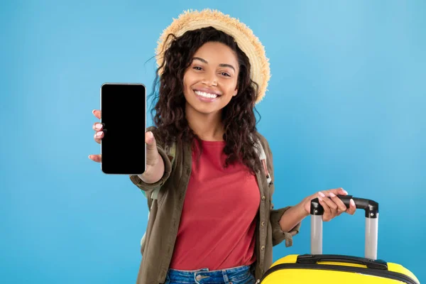 Junge schwarze Frau mit Koffer zeigt Smartphone vor Kamera, bietet Attrappe an, bucht Sommerurlaub online — Stockfoto