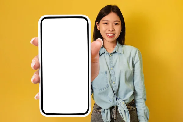 Junge Asiatin zeigt großes Smartphone mit Attrappe, wirbt für App oder Website, Werbeprodukt oder Dienstleistung — Stockfoto