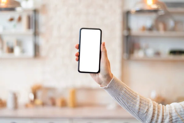 Primer plano de la mano femenina que muestra el teléfono inteligente con maqueta para la aplicación en línea o el diseño del sitio web en la pantalla en el interior de la cocina — Foto de Stock