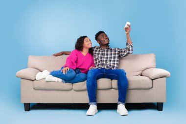 Sistemi ayır. Klima altında uzaktan kumandalı, mavi arka planda koltukta oturan genç siyah çift.