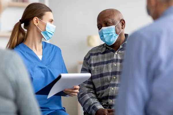 Pacientes mayores con máscaras faciales conversando con la enfermera — Foto de Stock